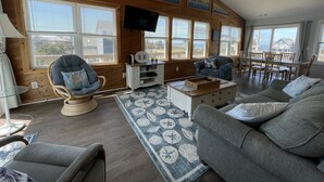 Un salón acogedor con techo alto, paredes de madera, un televisor de pantalla plana y un comedor con mesa y sillas.