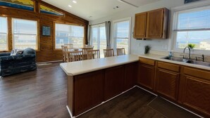 Una cocina con armarios de madera, un comedor con mesa y sillas, y ventanas amplias con vistas.