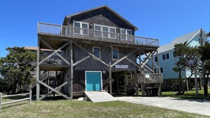 Un edificio de dos pisos con un balcón, un letrero que dice 'Hatteras Hideaway' y una puerta con marco azul.