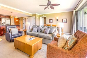 A hotel room with a sofa, armchair, and a wooden coffee table. There is a ceiling fan, a lamp, and a window with curtains. - Honua Kai | Ocean View 2 BR | Free Car w/ 6+ Nights | HKH-348 (Lahaina)