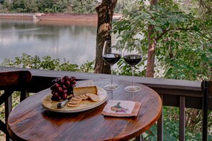 A round wooden table with a plate of cheese, grapes, and crackers, two wine glasses, and a napkin with a fruit design. - Walking Distance to Broadway! Fully Renovated Condo on the River, Free Parking (Nashville)