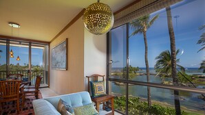 Un salón espacioso con un gran ventanal que ofrece vistas a palmeras y una masa de agua.