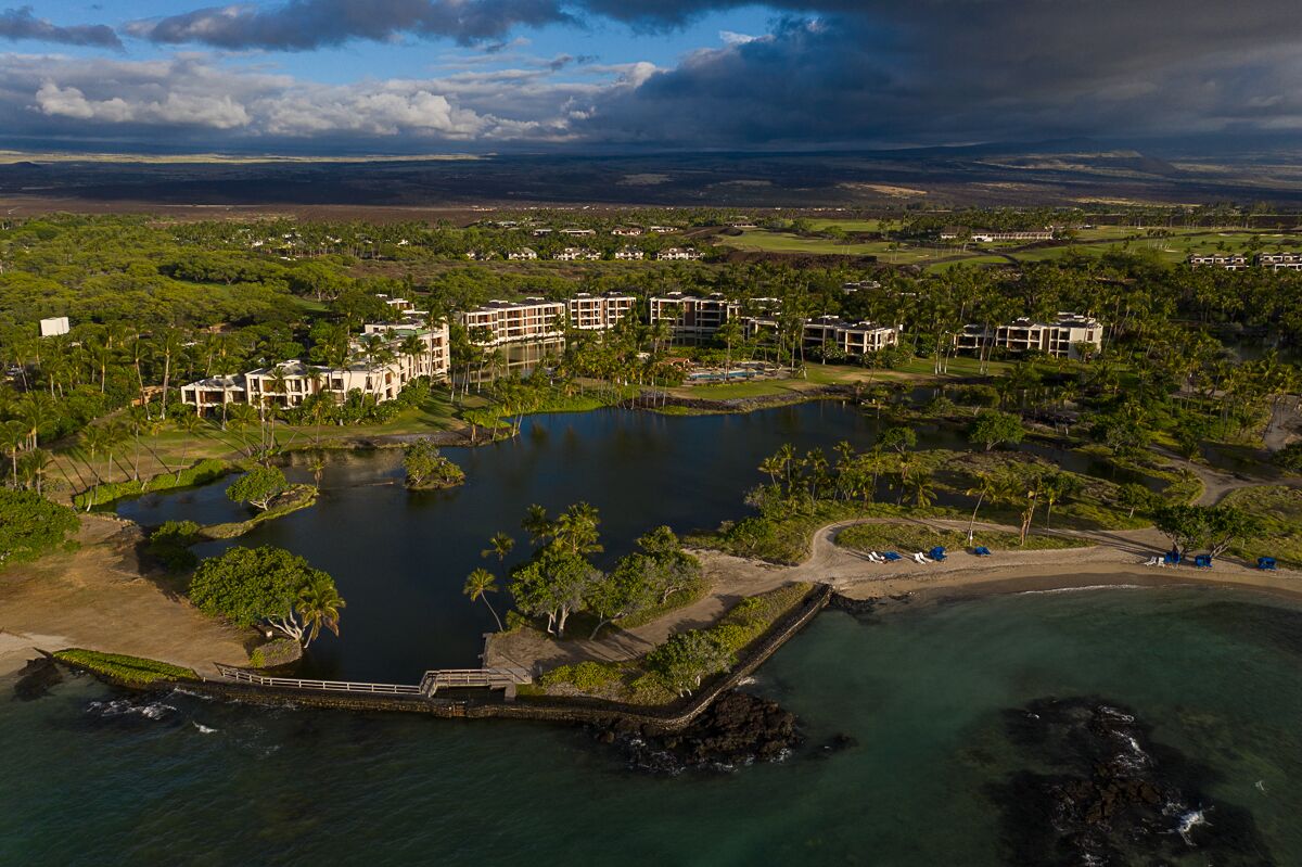 An aerial view of a resort with multiple buildings, a central water body, and surrounding greenery.