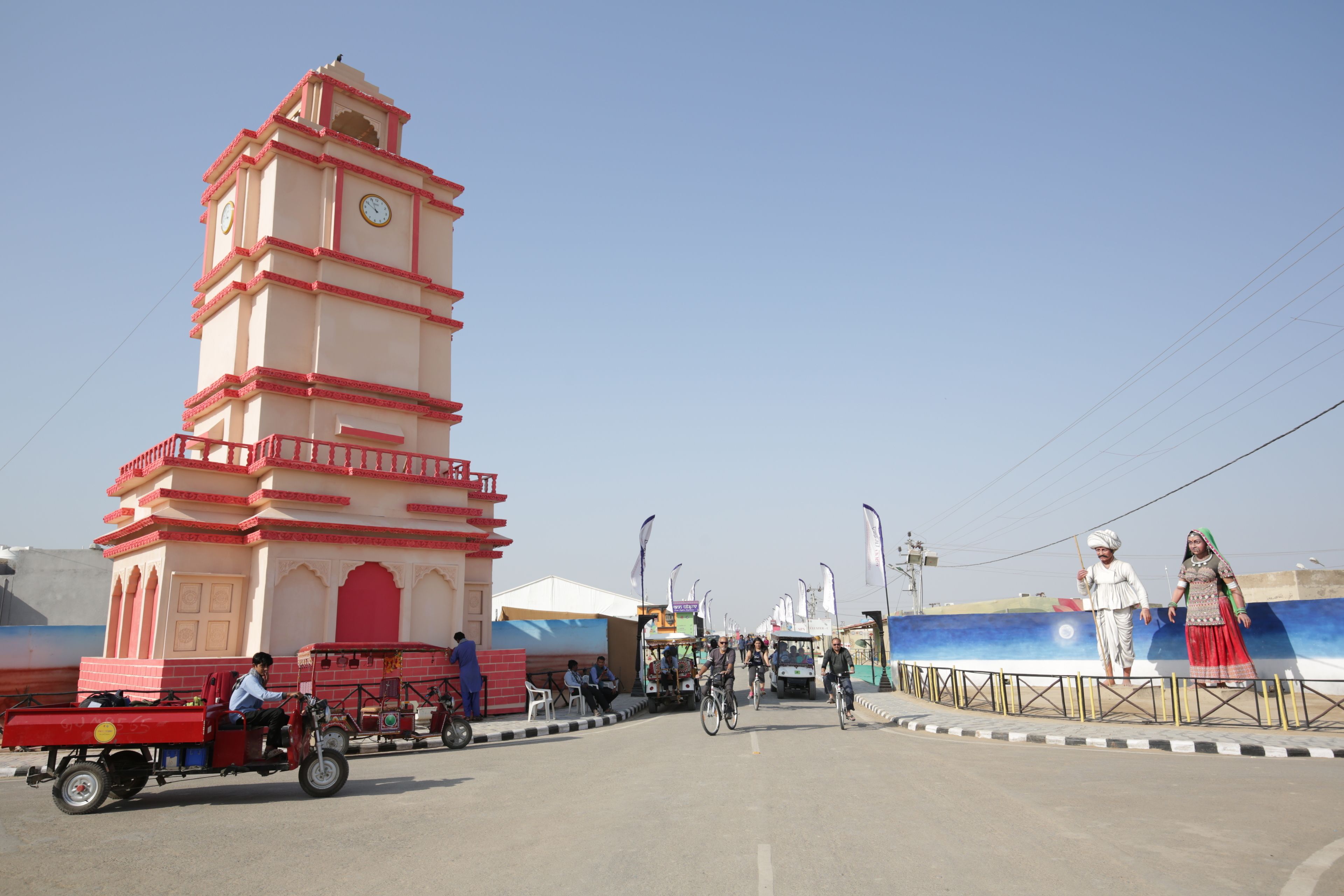 A tower with a clock, a street with people and vehicles, and a large banner with figures.