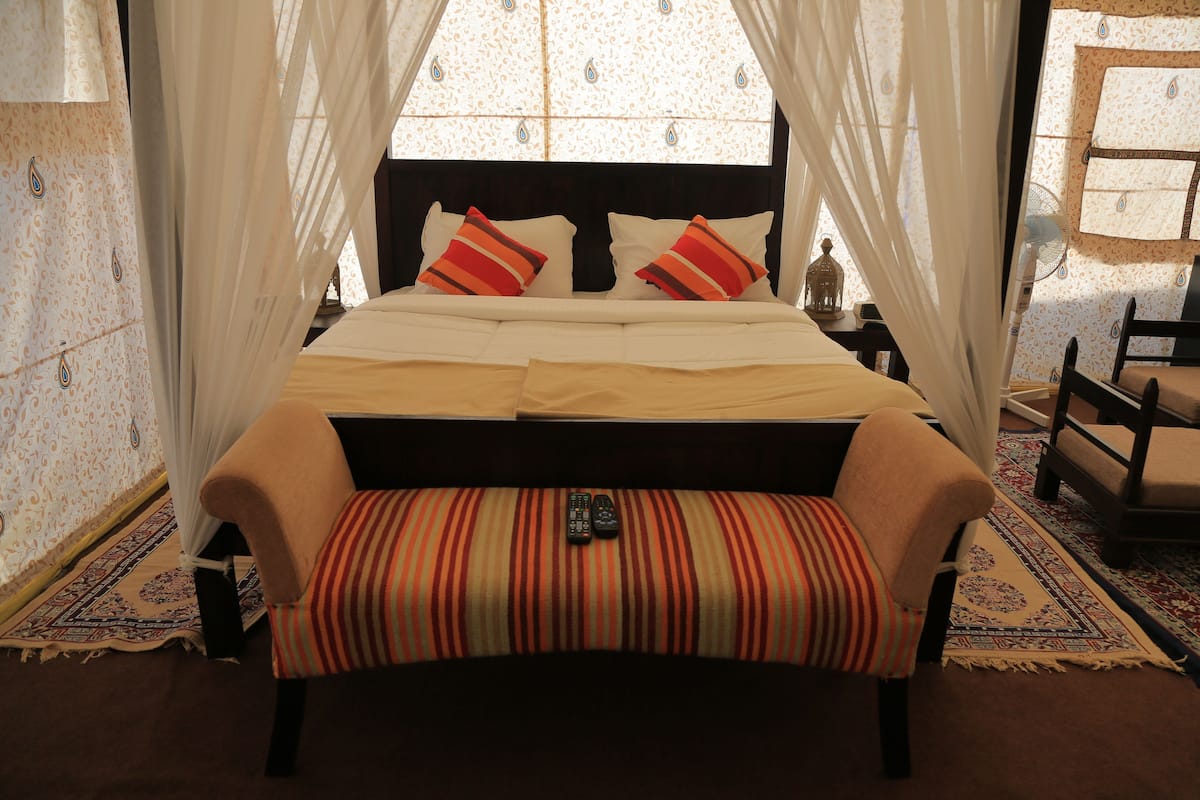 A bed with a canopy, pillows, and a bench.