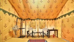 A tent-style room with two beds, a table, chairs, a fan, and a fire extinguisher. - Rann Utsav The Tent City (Bhuj)