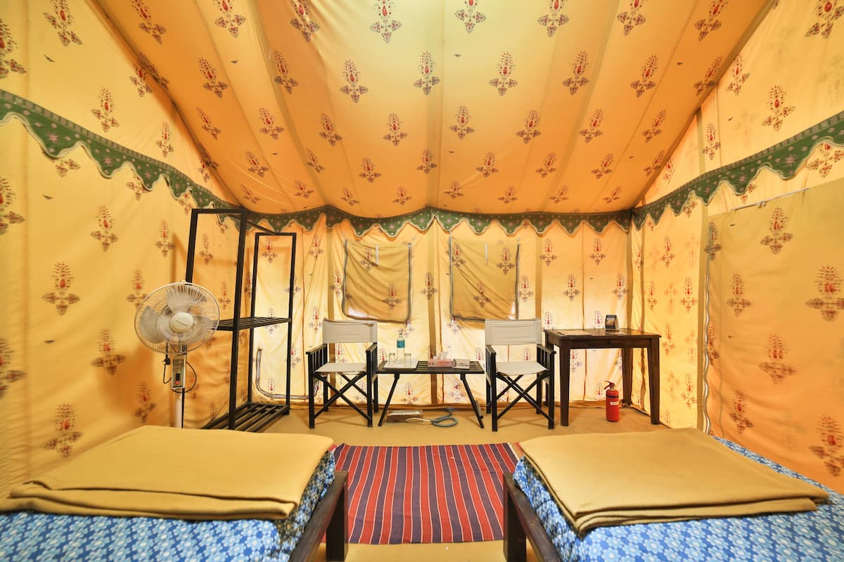 A tent-style room with two beds, a table, chairs, a fan, and a fire extinguisher.