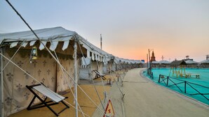 A row of tents with a pool and a lifeguard tower in the background. - Rann Utsav The Tent City (Bhuj)