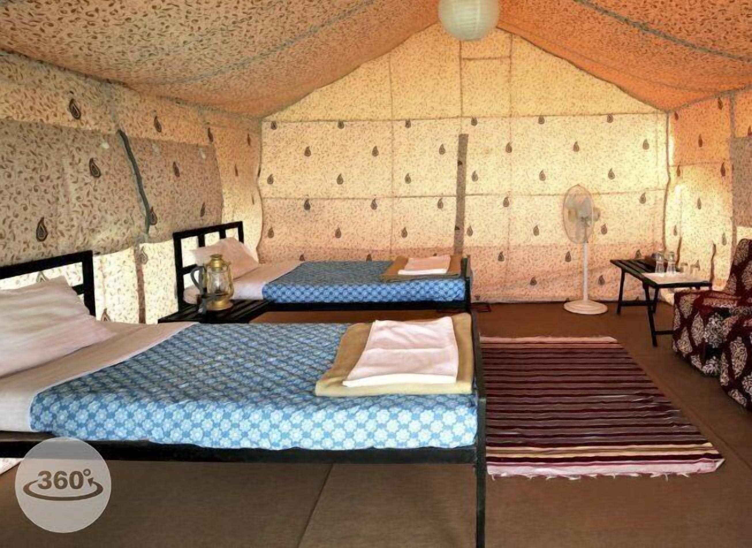 A tented accommodation with two beds, a fan, and a table with chairs.
