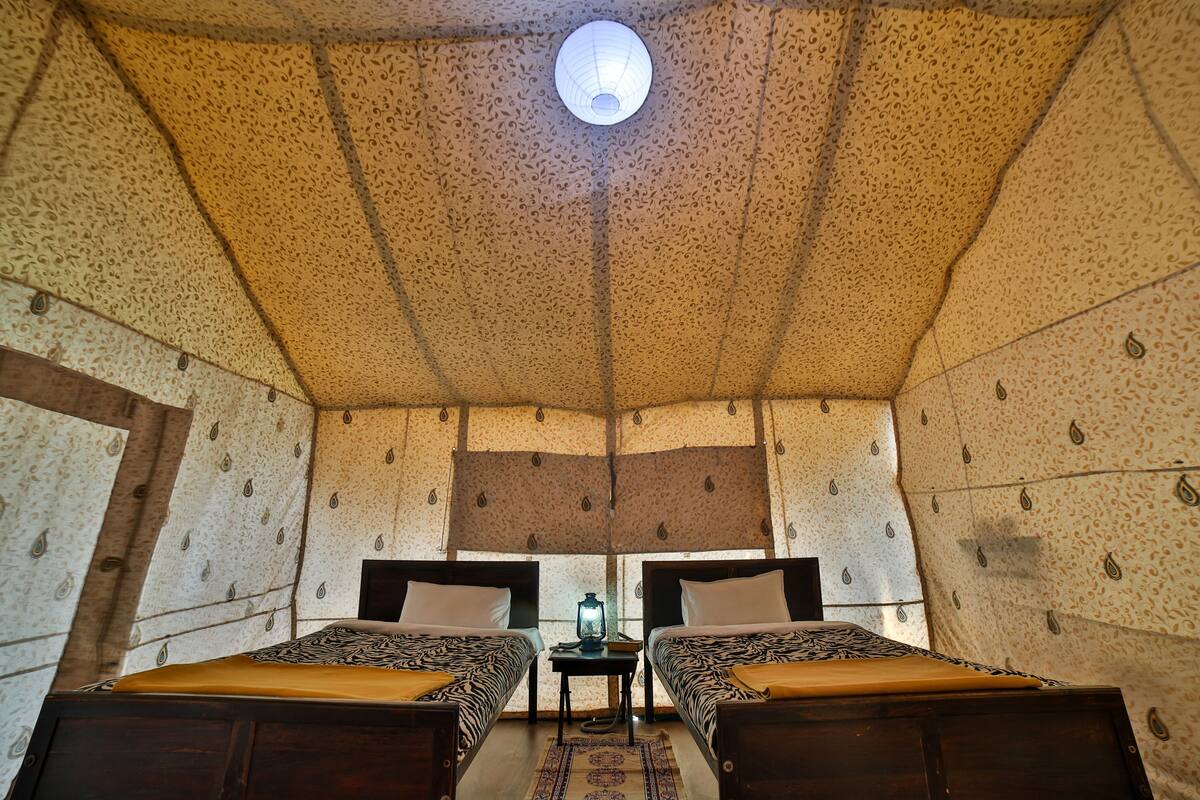 A room with two beds, a small table, and a hanging light fixture.