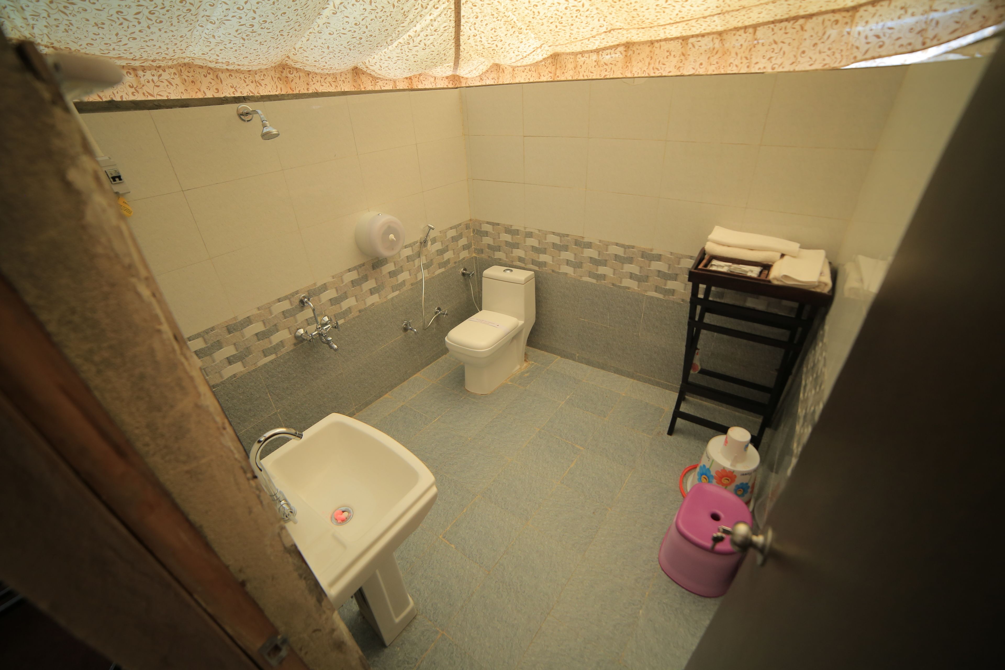 Un baño con inodoro, lavamanos, ducha y un pequeño estante con toallas.