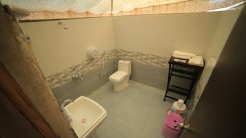 Un baño con inodoro, lavamanos, ducha y un pequeño estante con toallas.