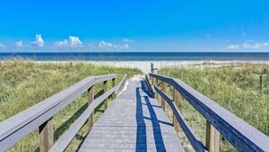 Une promenade en bois menant à une plage, avec un ciel dégagé.