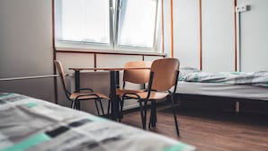 Une pièce comprenant un lit, un bureau, deux chaises et un radiateur.