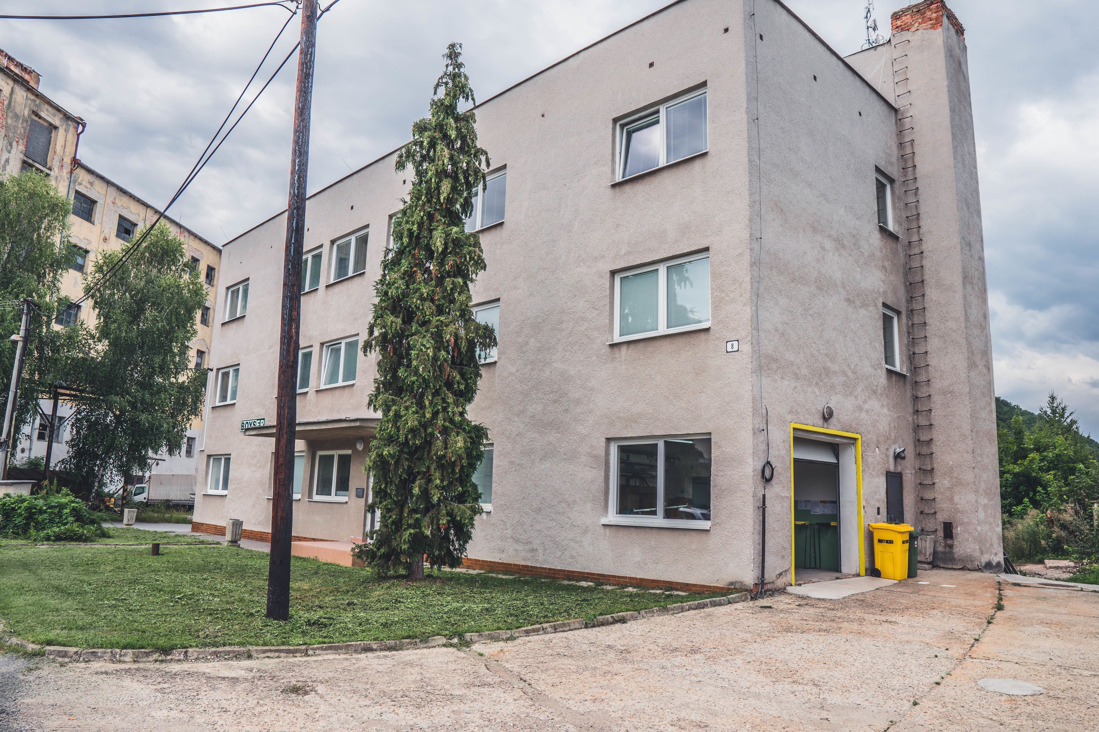 A multi-story building with a flat facade, a visible entrance with a yellow door, and a small grassy area in front.