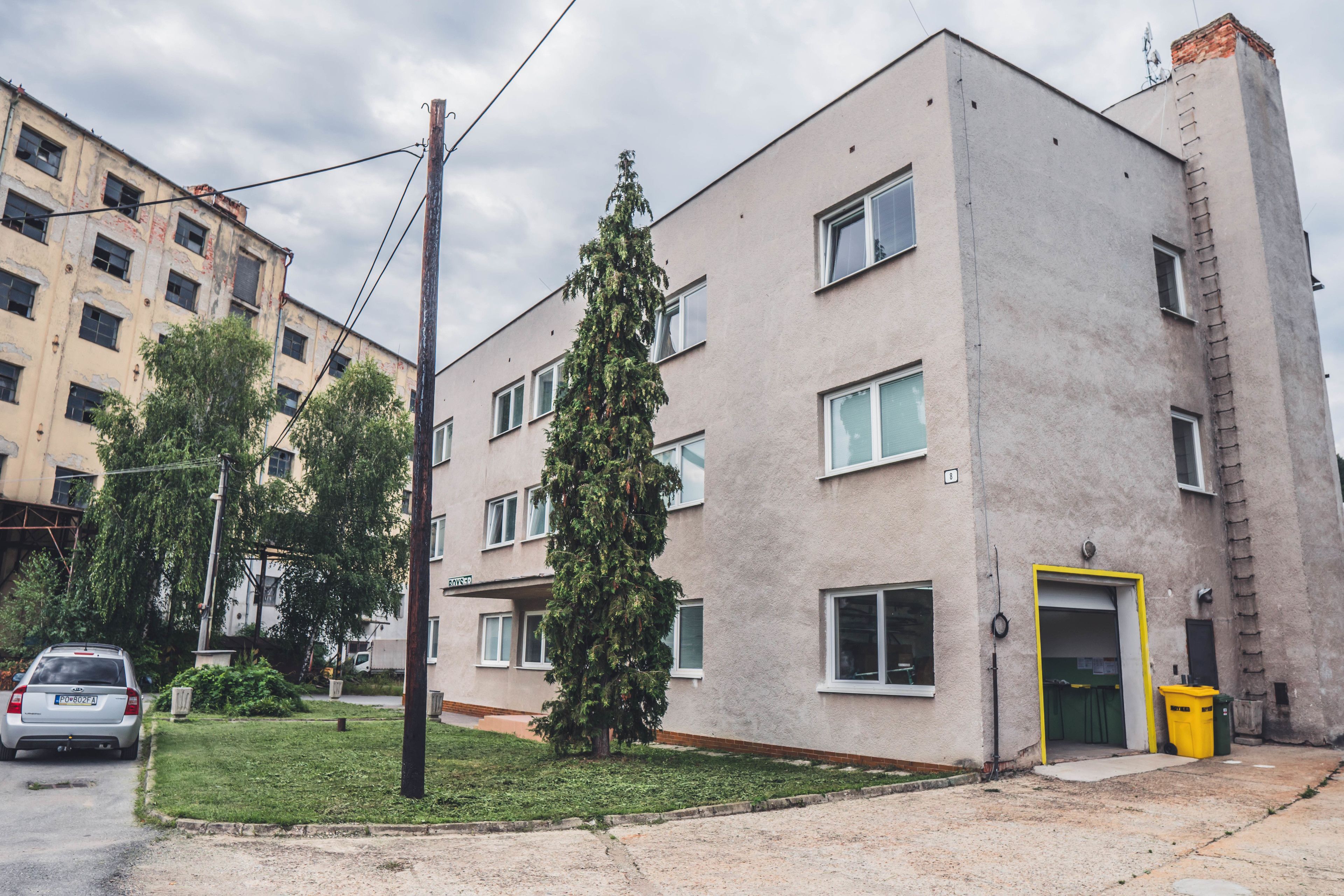 A multi-story building with a flat facade, a visible entrance with a yellow door, and a small green tree in front.