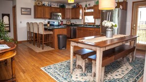 Une cuisine avec des meubles de rangement en bois, un réfrigérateur en acier inoxydable, une table à manger avec des bancs et une poubelle.