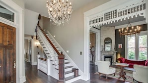 A spacious living area with a grand staircase, a fireplace, and a red sofa. - Southern Stunners - Large Group Luxury (Nashville)