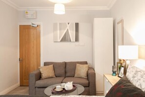 A living room with a sofa, a coffee table with teapots, a lamp, and a framed picture on a side table. - 11 Helena House (Reading)