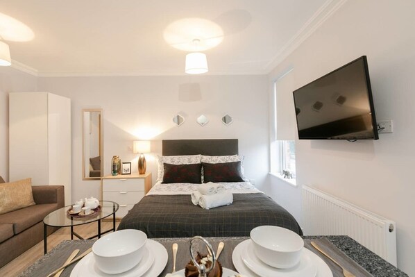 A modern hotel room with a bed, a TV mounted on the wall, a sofa, and a small table with tea cups. - 11 Helena House (Reading)