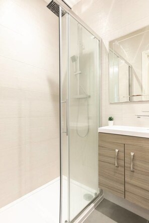 A modern bathroom with a glass-enclosed shower, a wooden vanity, and a large mirror above the sink. - 11 Helena House (Reading)