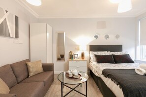 A modern bedroom with a bed, a sofa, a bedside table with a lamp, and a small round table with tea set. - 11 Helena House (Reading)