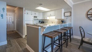 Cocina moderna con armarios blancos, encimera de mármol y una isla integrada con taburetes de bar.