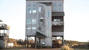 A multi-story building with a unique architectural design, featuring a combination of brick and glass elements. - Sunny Spot is a unique Oceanfront cottage in Frisco! (FRISCO)