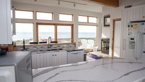 A modern kitchen with large windows, a marble countertop, and a view of the ocean. - Sunny Spot is a unique Oceanfront cottage in Frisco! (FRISCO)