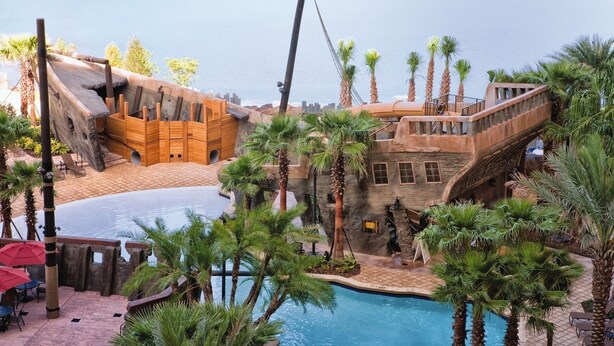 A pool area with a wooden ship structure, palm trees, and a clear view of the water.