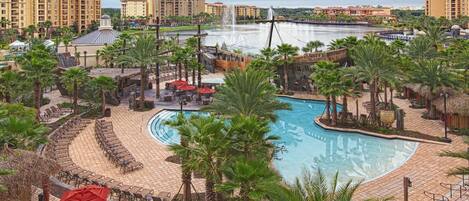 A resort with a central pool, palm trees, and a view of distant buildings.