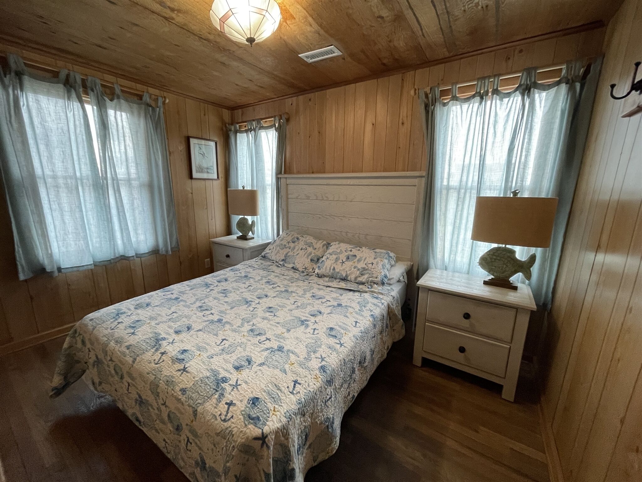 A wooden-paneled bedroom with a bed, two nightstands, and a ceiling light fixture.