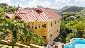 Un immeuble jaune à plusieurs étages, surmonté d’un toit rouge, entouré de verdure et agrémenté d’une piscine.
