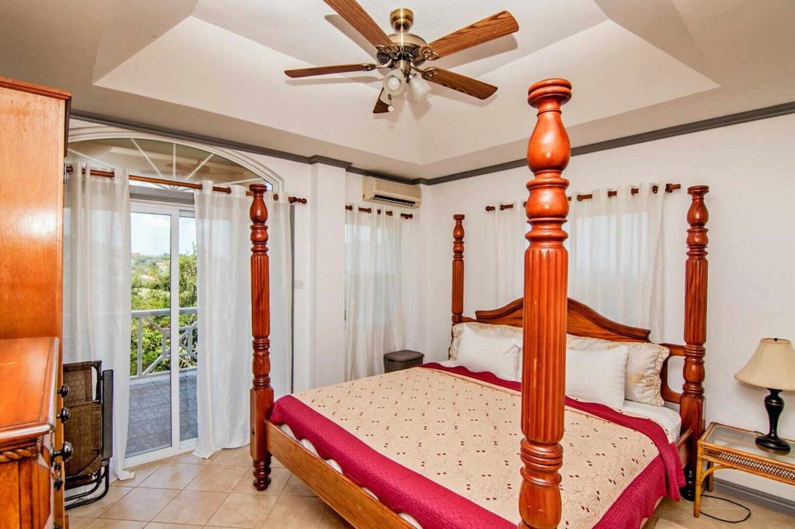 A four-poster bed with a wooden headboard, a ceiling fan, and a view through a glass door to the outside.