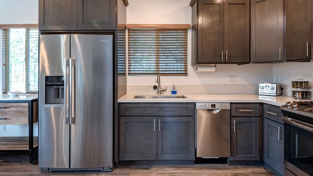 A modern kitchen with dark wood cabinets, stainless steel appliances, and a built-in dishwasher.