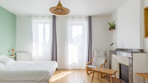 A bedroom with a bed, a chair, a table, a fireplace, and a hanging light fixture.