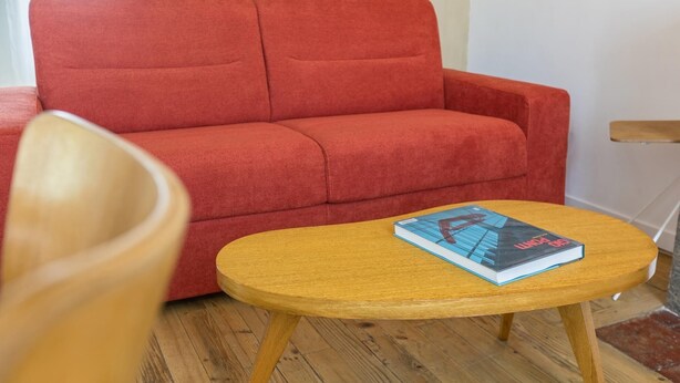 A red sofa and a small wooden table with a book on it in a room with wooden flooring. - Le Passage - bright apartment with terrace (Albi)