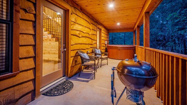 A wooden cabin with a balcony, a hot tub, and a grill.