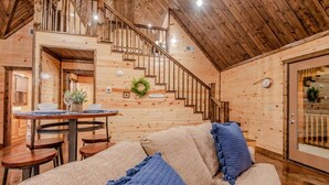 A cozy wooden interior with a staircase, a dining area, and a sofa with blue cushions.