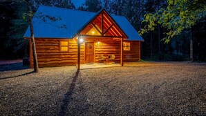 A log cabin with a metal roof, a porch with a chair, and a gravel driveway.