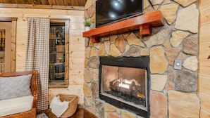 A cozy living room with a stone fireplace, a mounted TV, and a wicker chair.