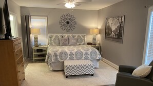A bedroom with a bed, bedside lamps, a ceiling fan, a dresser, a chair, and a wall-mounted artwork. - Lake Greenwood, Big Water and Sunset Views (Chappells)