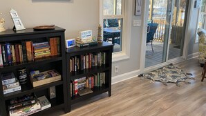 A living room with a bookshelf, a painting, and a view of the outdoors through a sliding glass door. - Lake Greenwood, Big Water and Sunset Views (Chappells)