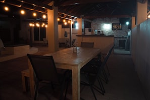 A dining area with a long wooden table and chairs, a stone wall, and a kitchen in the background. - LiCe 's Garden Aruba (Paradera)