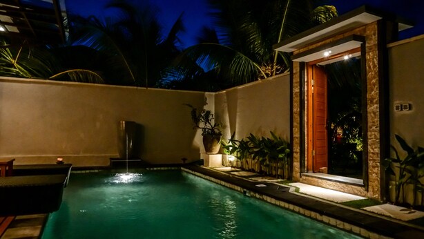 Une piscine agrémentée d’un élément décoratif aquatique, entourée de plantes et bordée d’un mur en pierre.