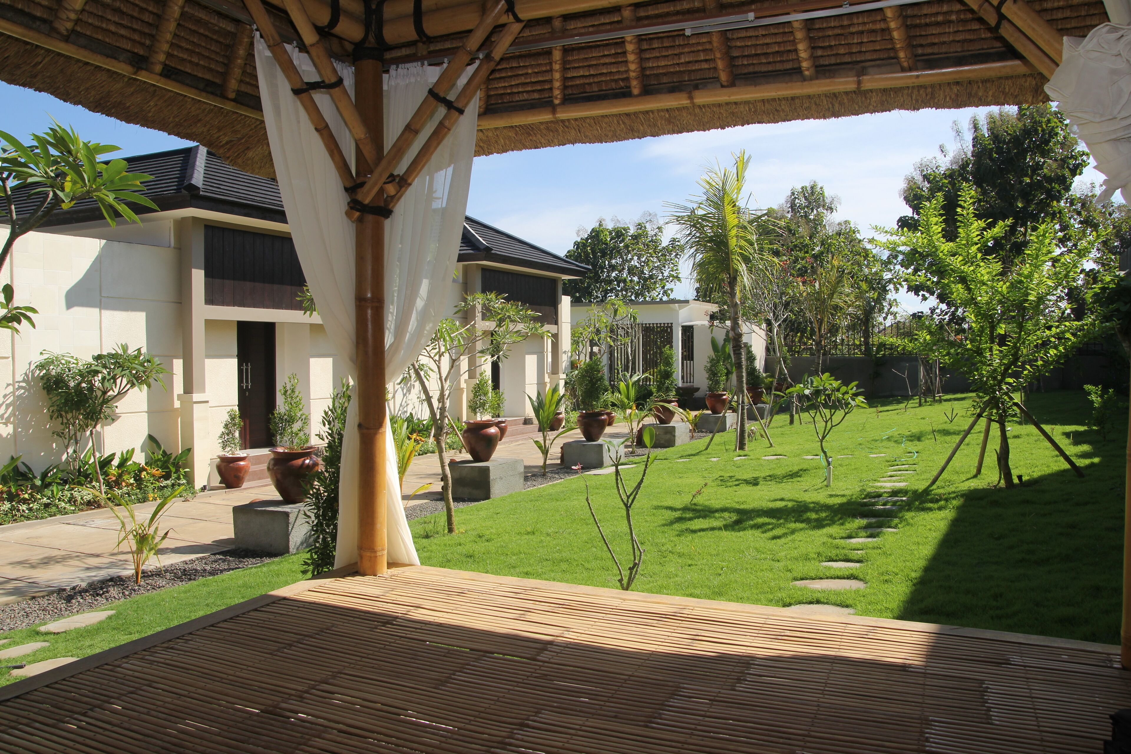A covered outdoor area with a wooden deck, potted plants, and a well-maintained lawn.