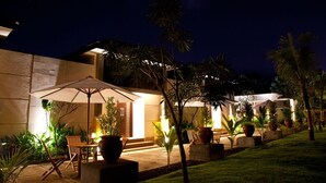 Un espace extérieur aménagé en terrasse, avec des sièges et des parasols, entouré de palmiers et de plantes en pot.