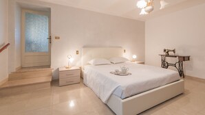 Een slaapkamer met een bed, nachtkastjes, een naaimachine en een deur met een geëtste glazen ruit.