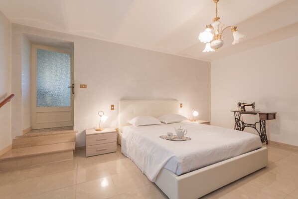 A bedroom with a bed, bedside tables, a sewing machine, and a door with a frosted glass panel.