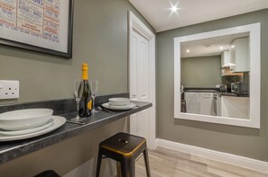 A modern kitchen with a grey wall, white cabinets, and a large mirror.